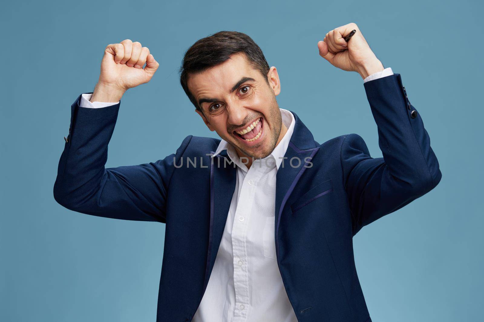 man holds hands above head with open mouth emotion official blue background. High quality photo