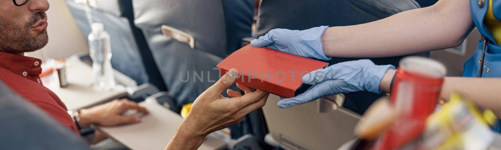 Close up shot of hands of male passenger getting lunch box from female flight attendant serving food on board. Travel, service, transportation, airplane concept