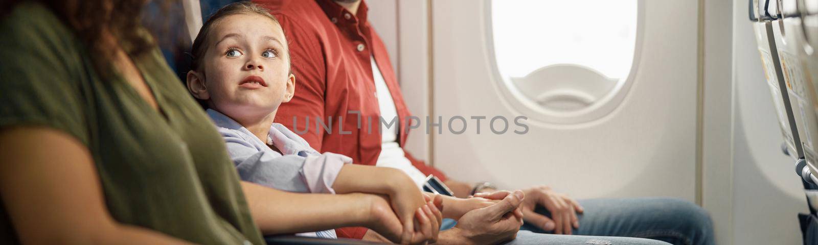 cheerful caucasian family, parents with little daughter holding hands together while sitting on the airplane. Transportation concept