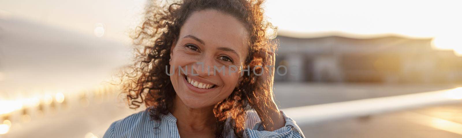 Portrait of happy female tourist, cheerful woman smiling at camera while standing outdoors ready for boarding the plane at sunset. Vacation, lifestyle, traveling concept