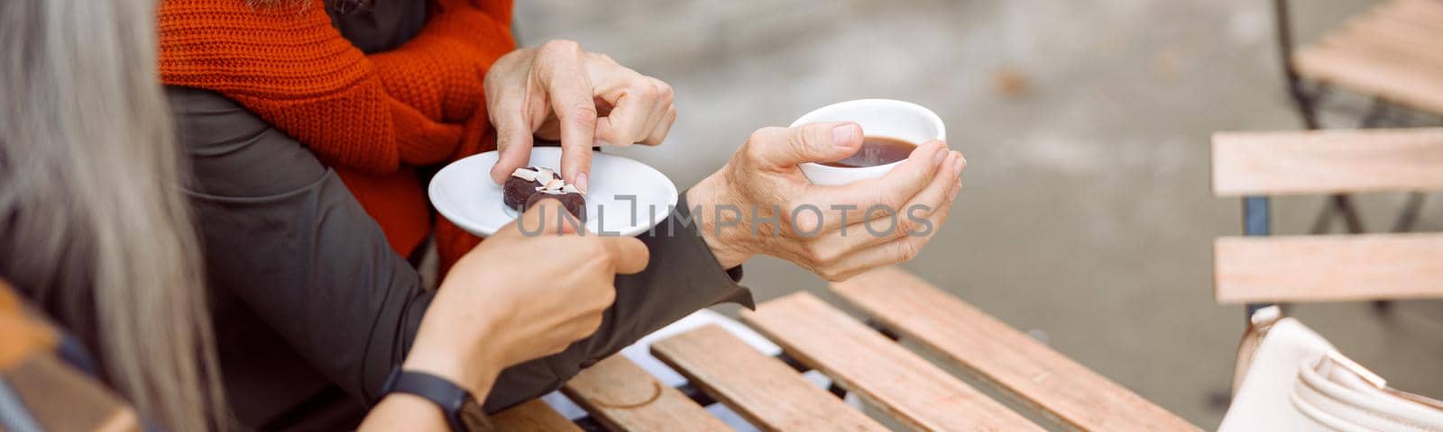 Happy mature woman takes candy from friend at wooden table in street cafe by Yaroslav_astakhov