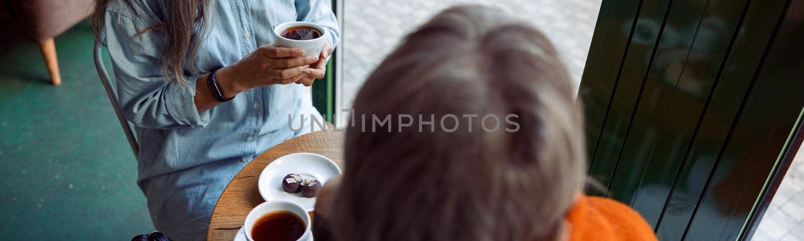 Happy senior Asian woman with grey haired friend look through window sitting at small table in cozy cafe. Long-time friendship