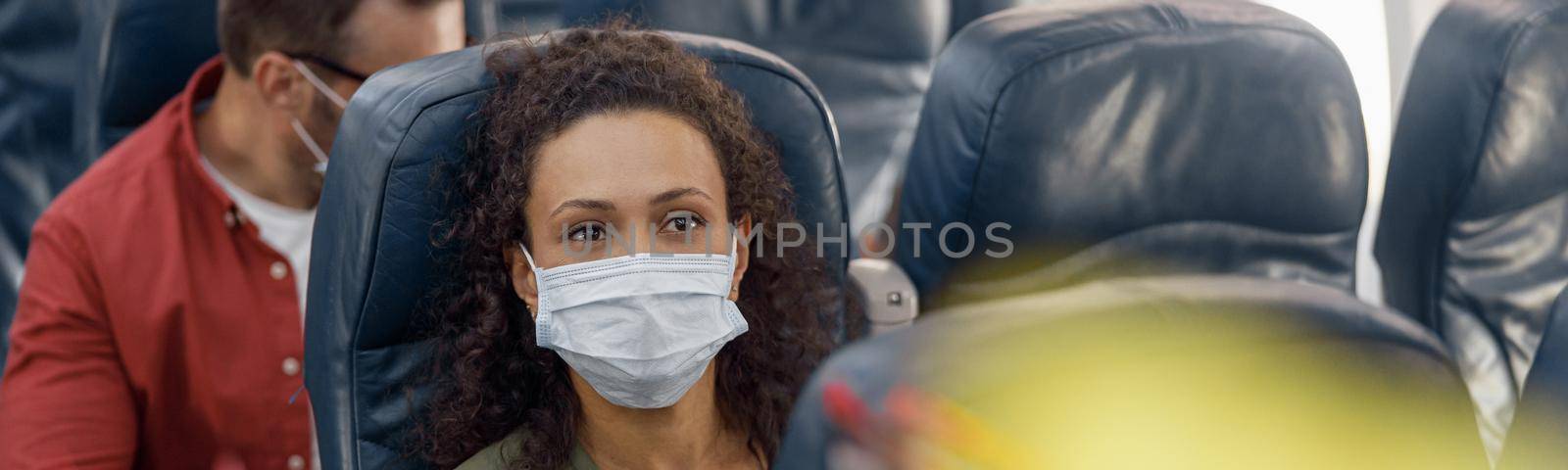 Female passenger wearing protective face mask waiting for stewardess to order coffee during the flight. Covid19, travel, service, transportation, airplane concept. Selective focus