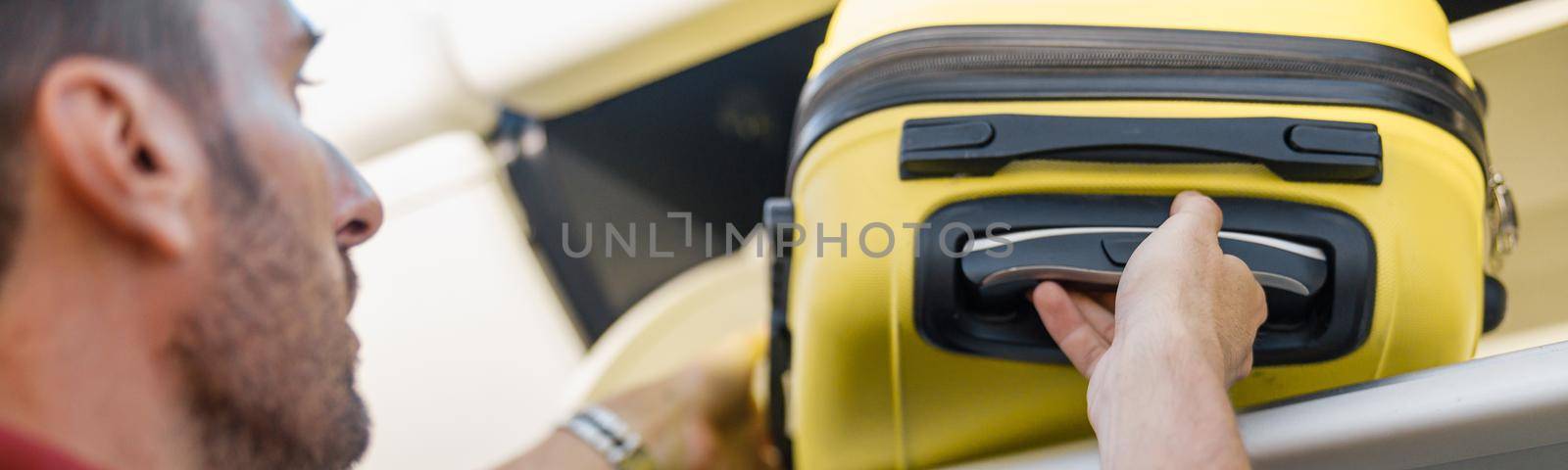 Man pulling out hand luggage from compartment while traveling by plane by Yaroslav_astakhov