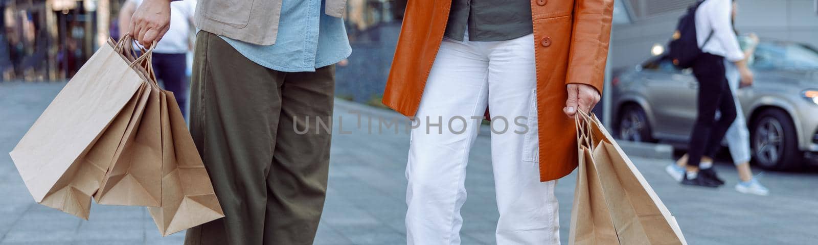 Pair of senior ladies holds shopping bags standing on modern city street on autumn day closeup. Friends spend time together
