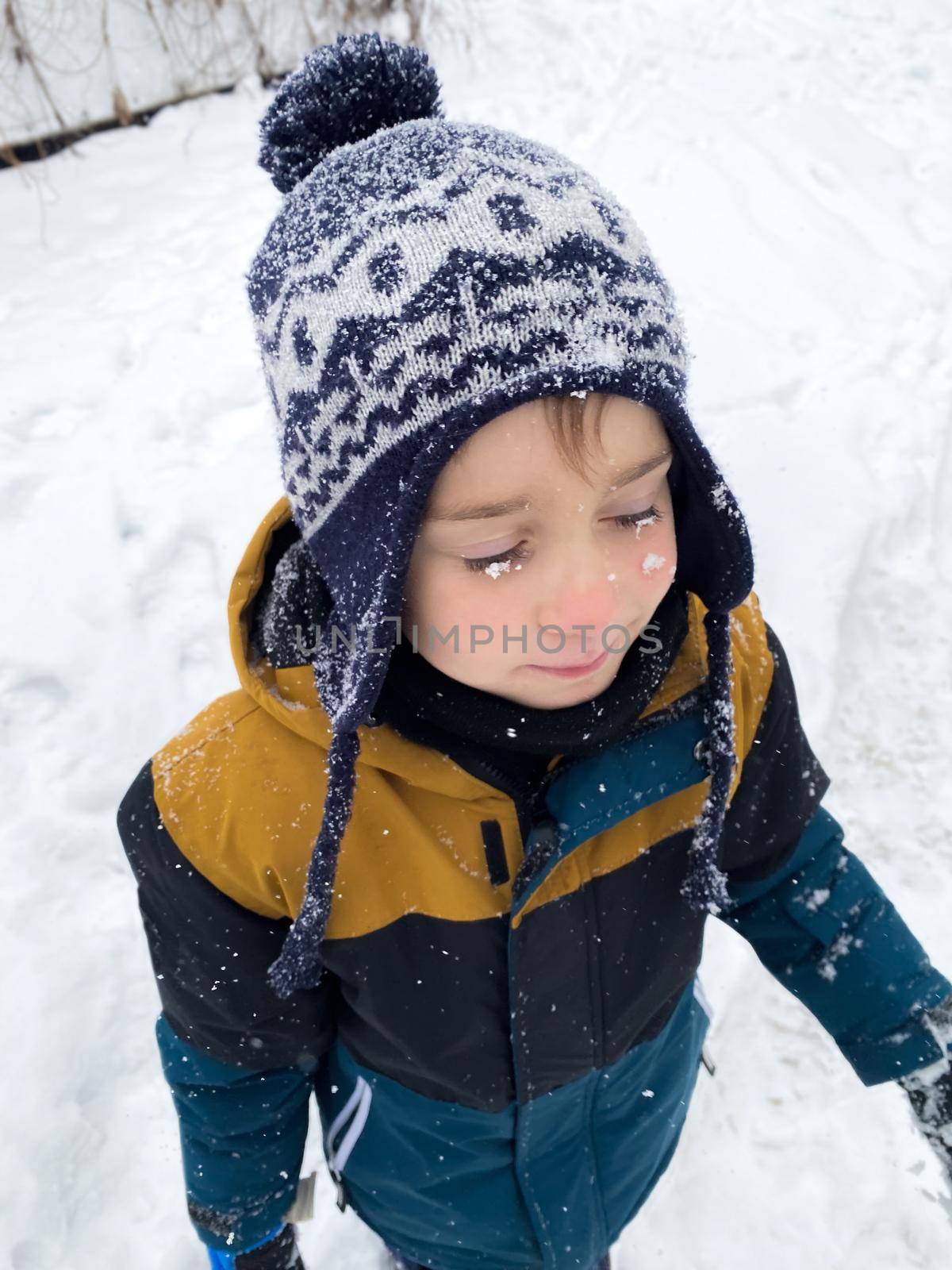 Portrait of a happy five year old boy in the snow in winter. Snowflakes on the hat and eyelashes