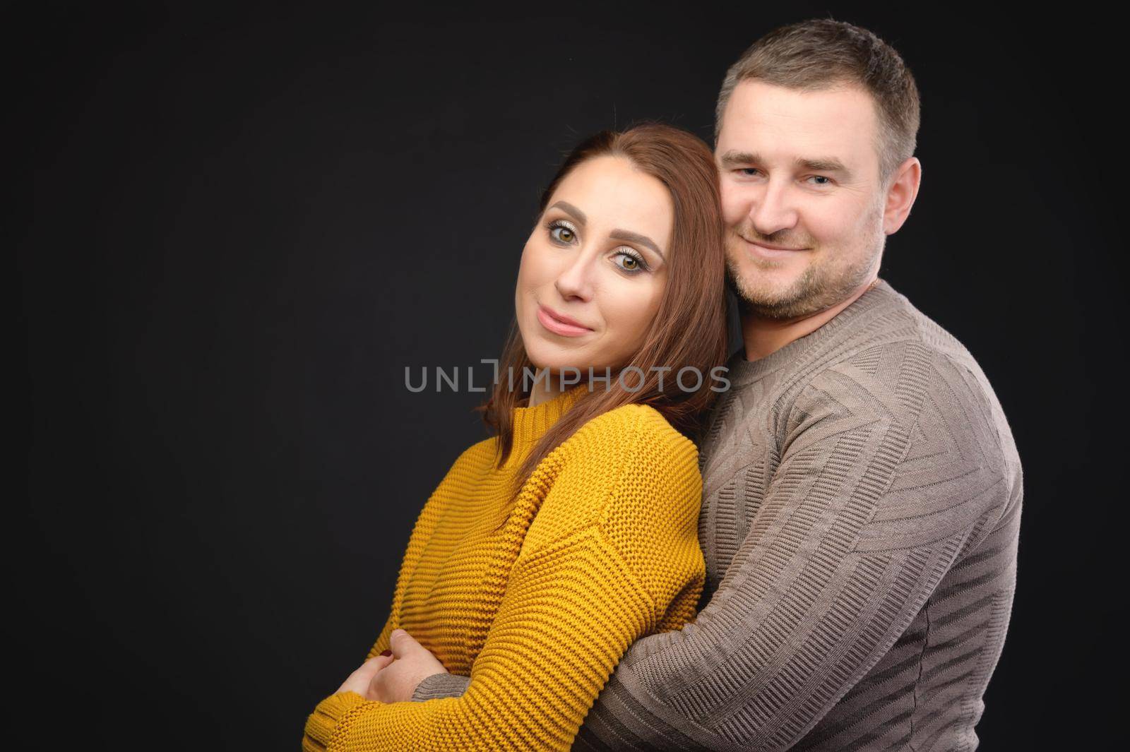 portrait of a happy caucasian family couple, stand and hug in a photo studio on a black background