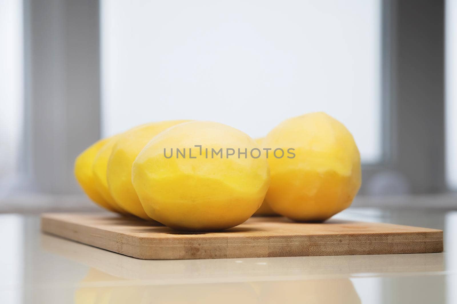 Several peeled potatoes on a wooden cutting board on a white table