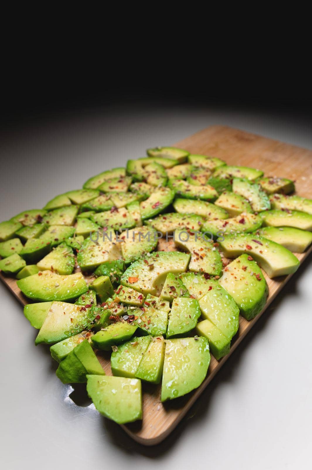 Wide Angle Large slices of sliced ripe avocado lie textured on a wooden cutting board. Sprinkled with spices. Healthy food. Vegetarianism.