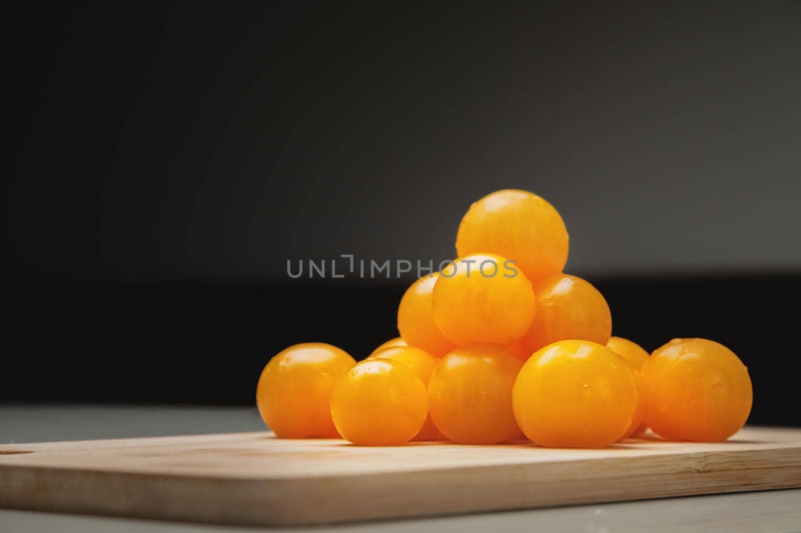 A heap of yellow cherry tomatoes on a wooden cutting board in the kitchen on a white table by yanik88