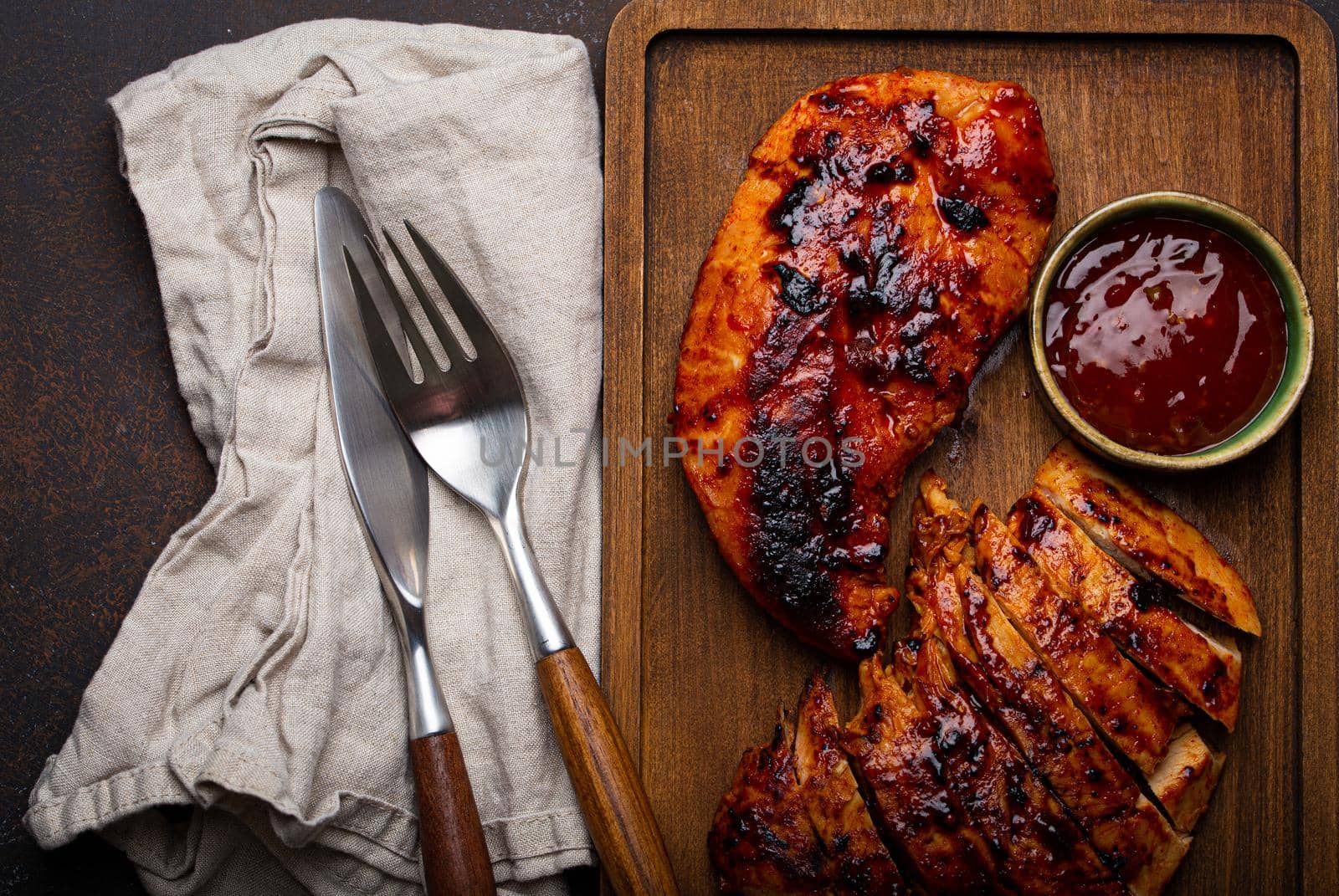 Grilled turkey or chicken marinated fillet with red sauce served and sliced on wooden cutting board on stone brown background from above, poultry breast barbecue