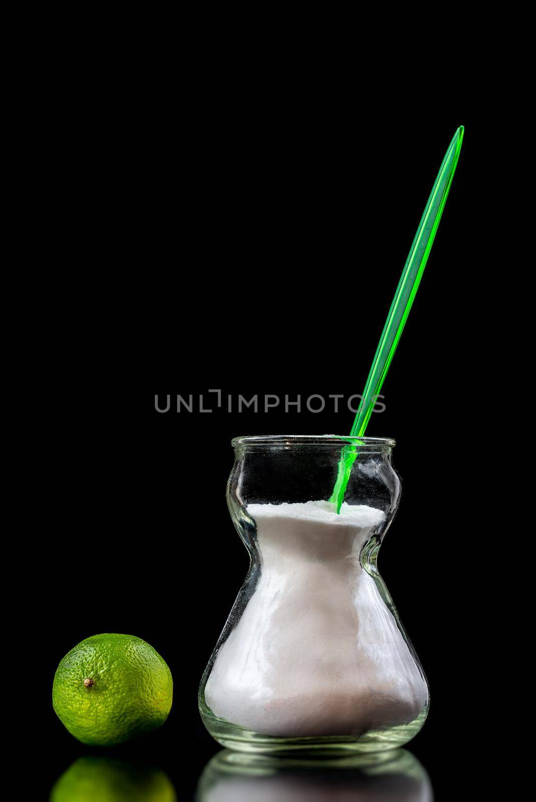 Jar of bicarbonate next to a lime in hard close-up a cropped black background