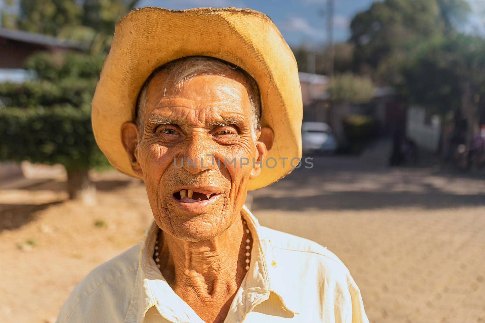 Latin old man without teeth and wearing a hat smiling and looking at the camera during a sunny day in Nicaragua.
