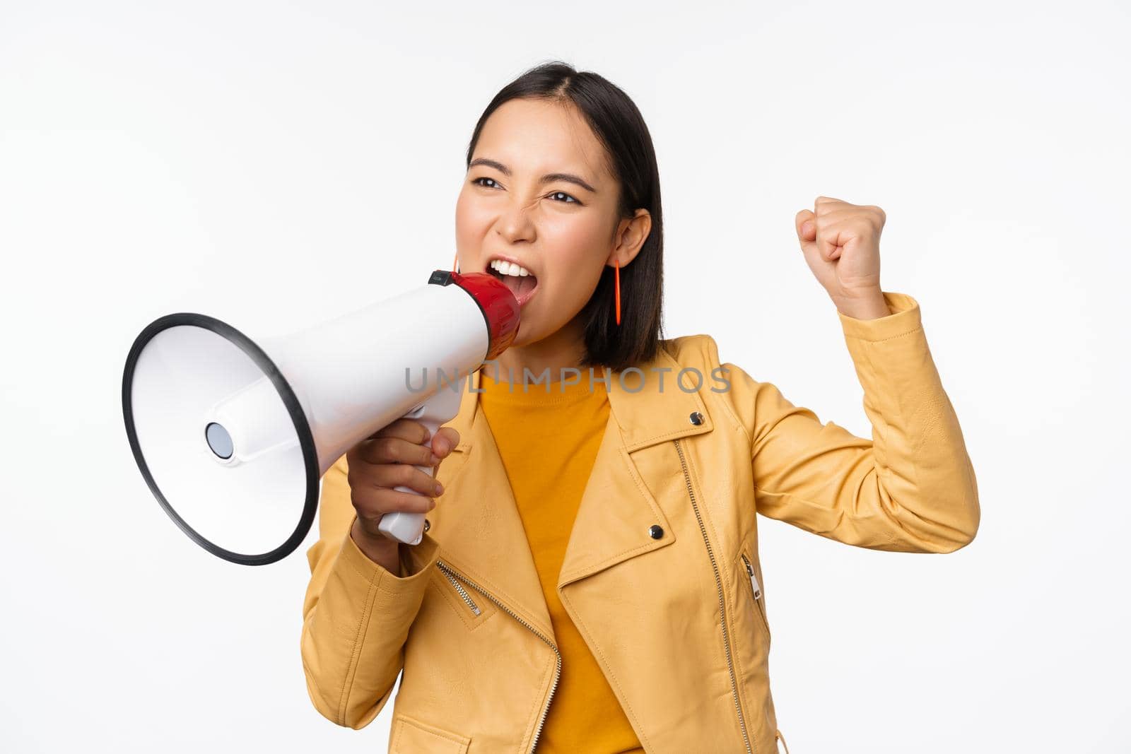 Portrait of young asian woman protester, screaming in megaphone and protesting, standing confident against white background.