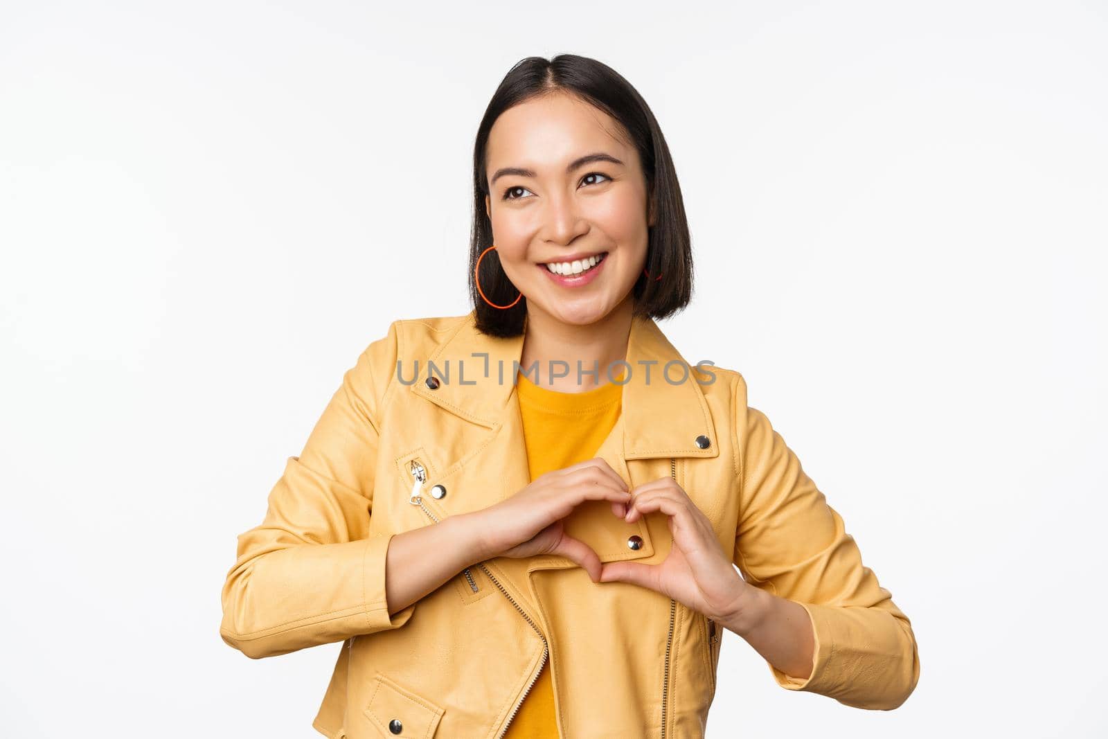 Image of beautiful asian girl showing heart, love sign, express care and romantic feelings, standing over white studio background by Benzoix
