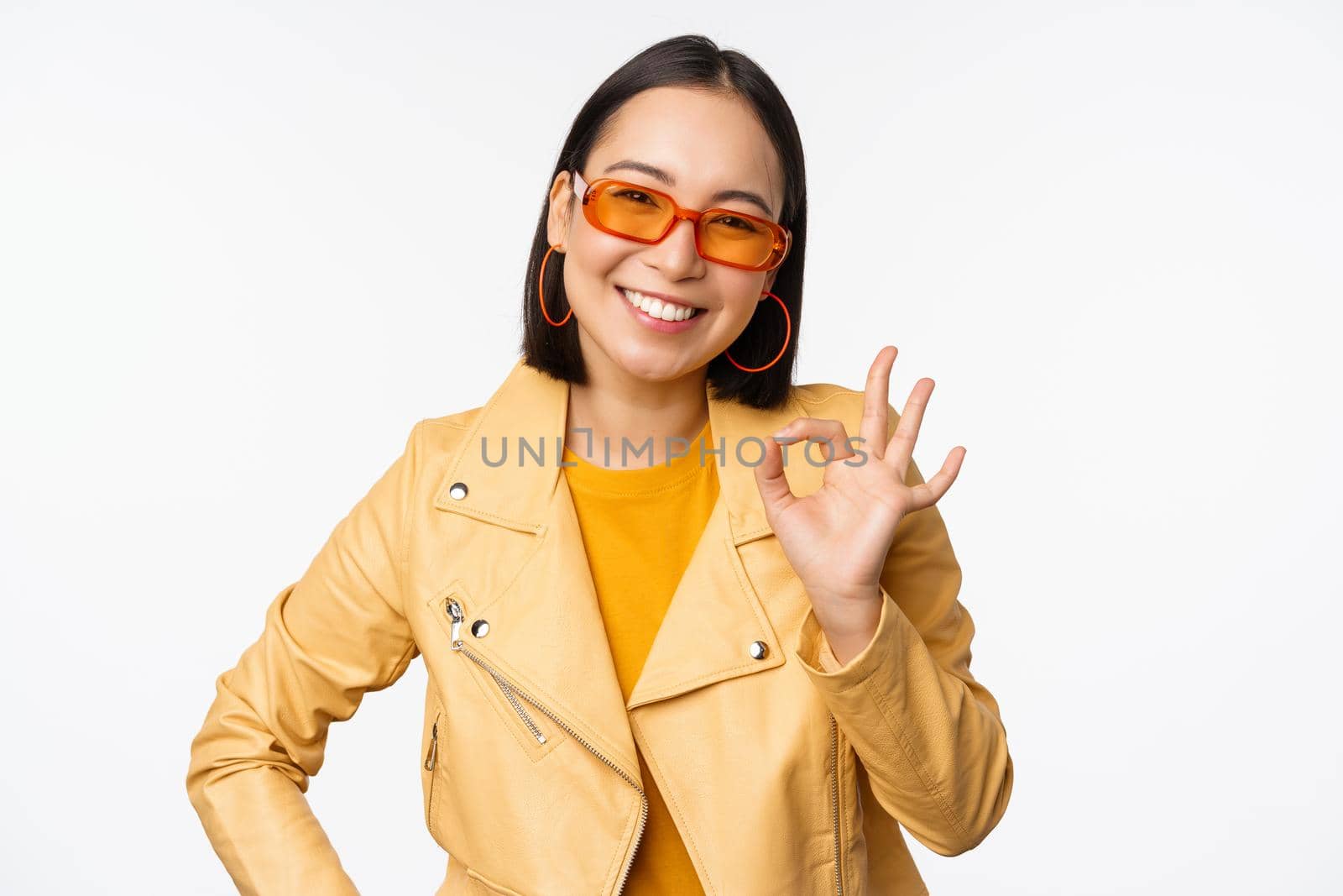 Excellent. Smiling asian girl shows okay, ok sign, nod in approval, recommending smth good, standing over white background. Copy space