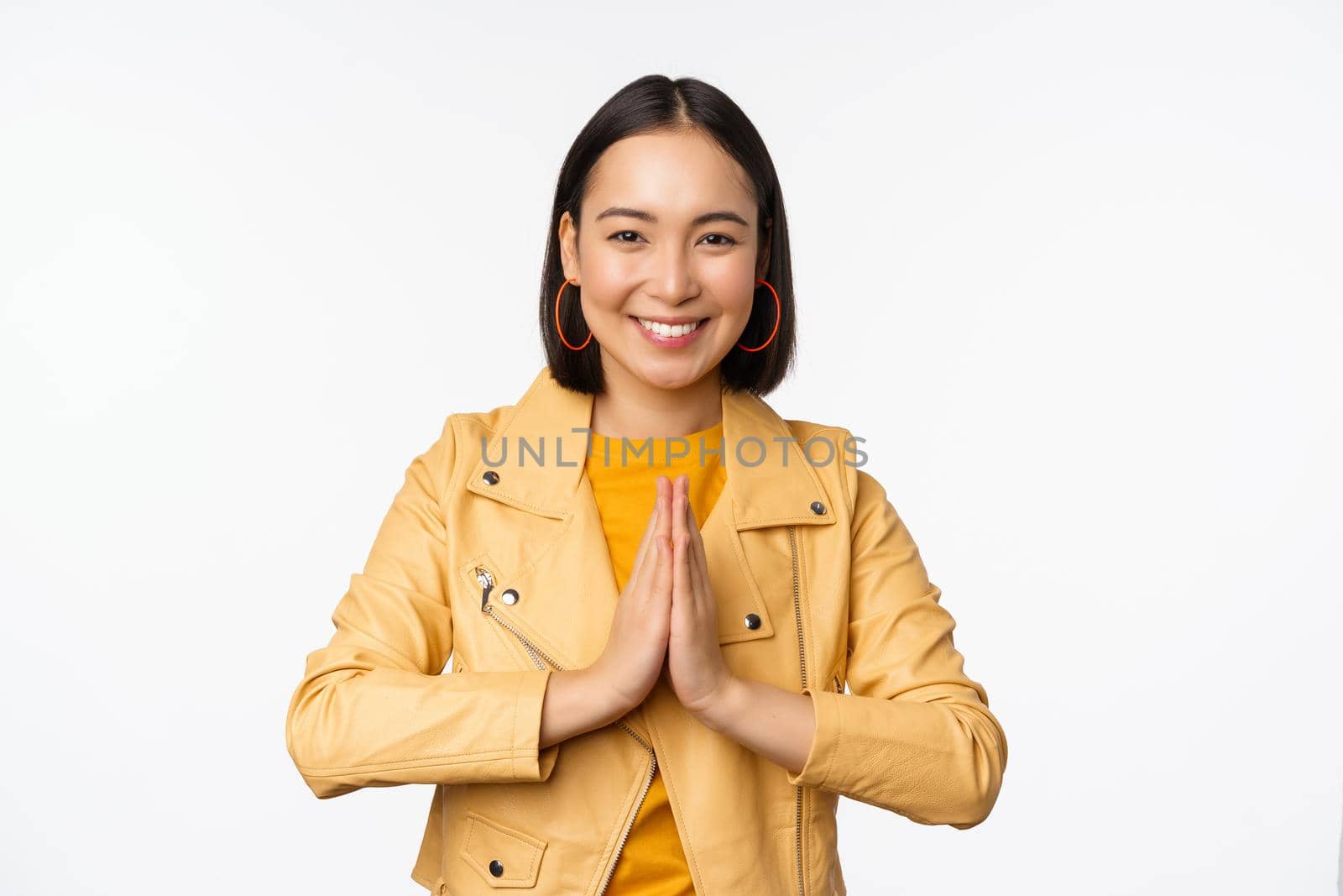 Happy korean woman, looking hopeful, asking for help favour, begging, standing with namaste gesture and smiling, standing over white background.
