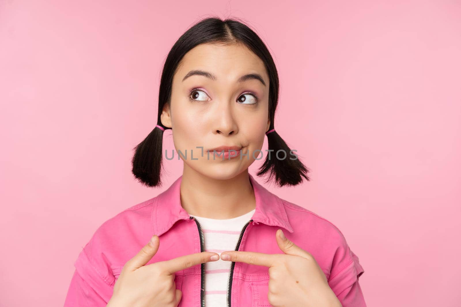 Cute korean girl with silly hairbuns, looking happy and shy, thinkin of smth, posing against pink background by Benzoix