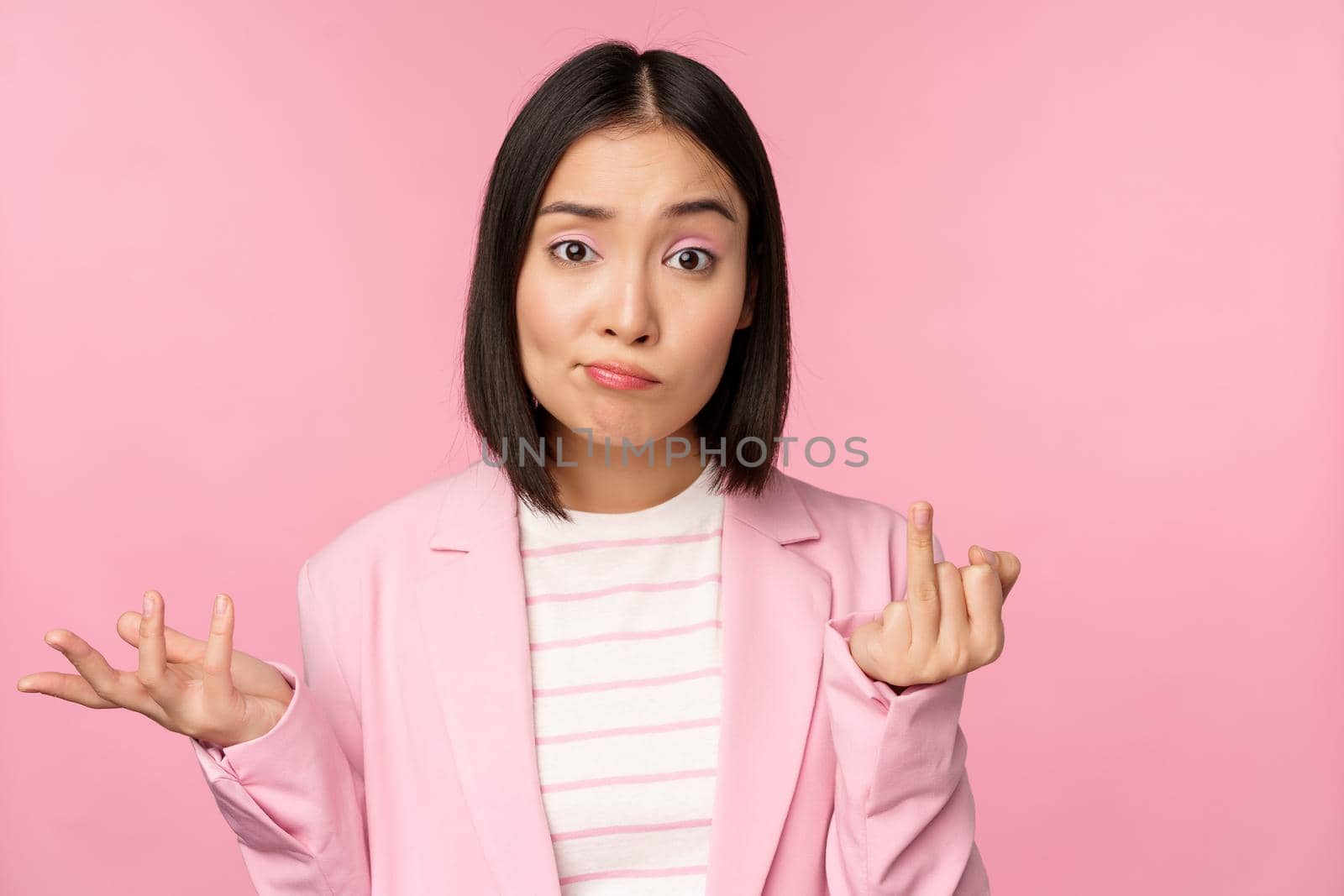 Portrait of young asian business woman, saleswoman shrugging shoulders and looking confused, clueless of smth, standing over pink background by Benzoix