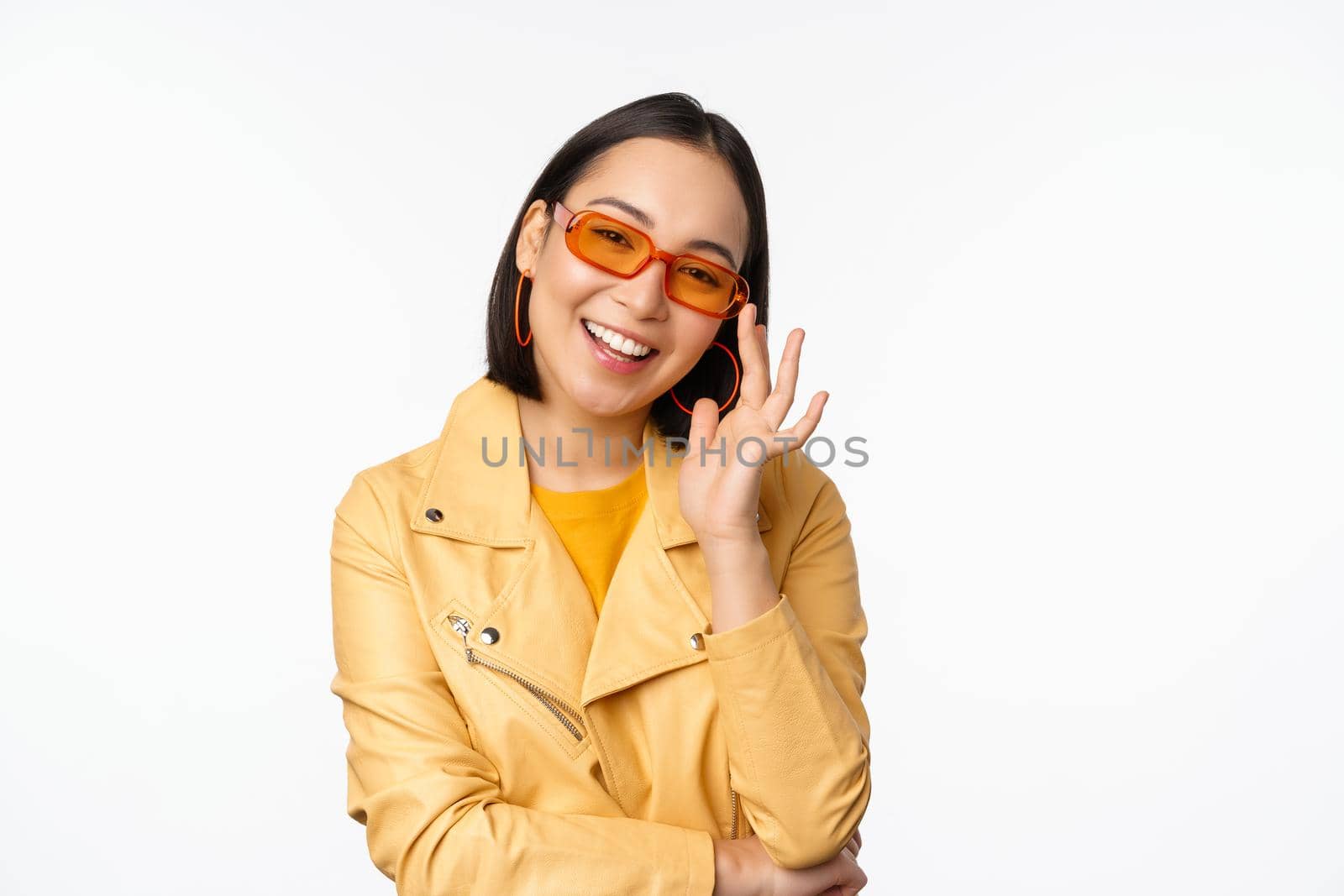 Stylish asian girl in sunglasses, smiling and looking cool, standing over white background.