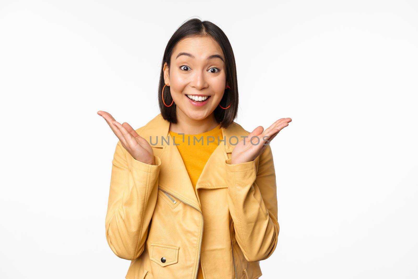 Image of asian woman looking surprised, amazed reaction, shocked face, standing over white background. Copy space