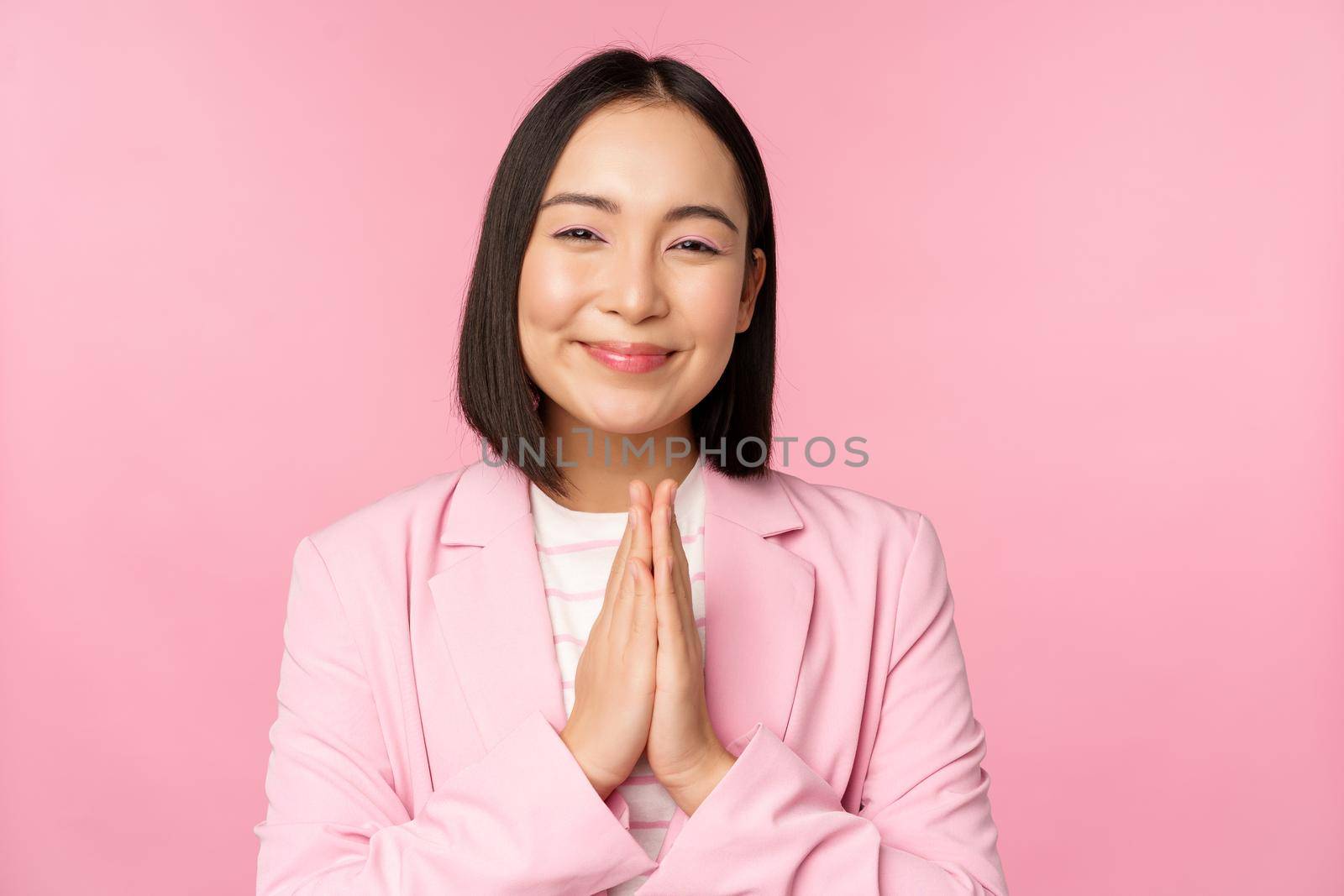 Thank you. Smiling asian saleswoman, corporate lady in suit thanking, holding hands in bag, gratitude gesture, standing over pink background by Benzoix