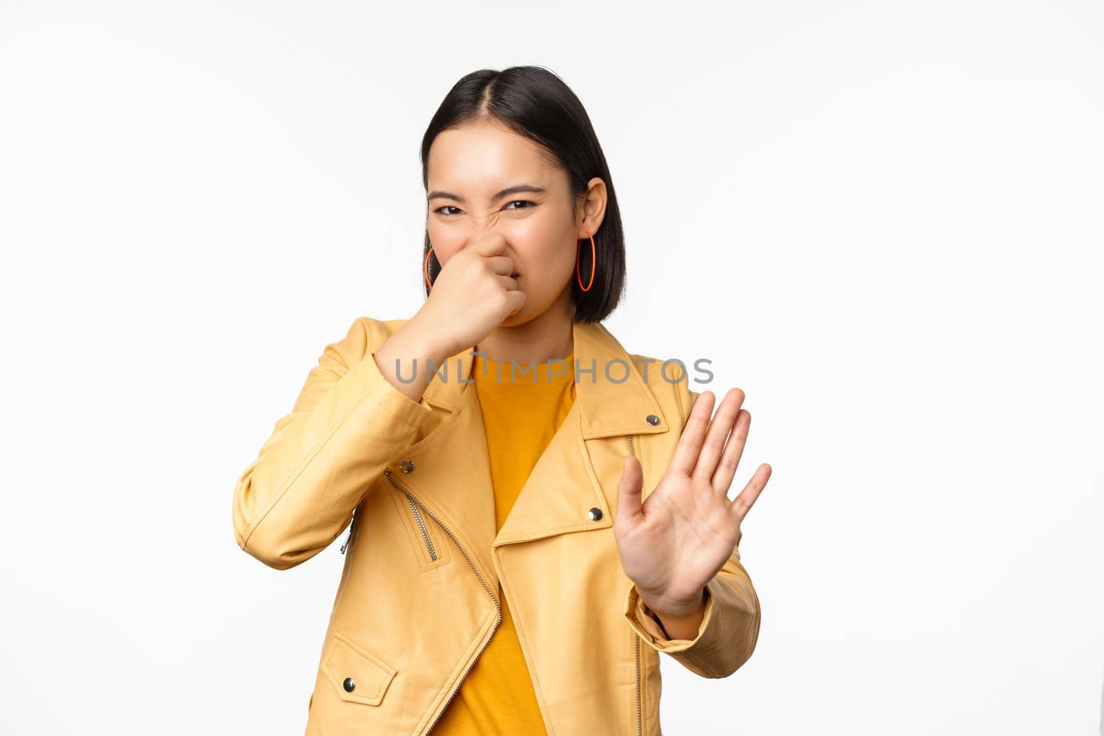 Image of asian girl shuts nose and reject smth with disgusting bad smell, shuts nose, standing over white background by Benzoix