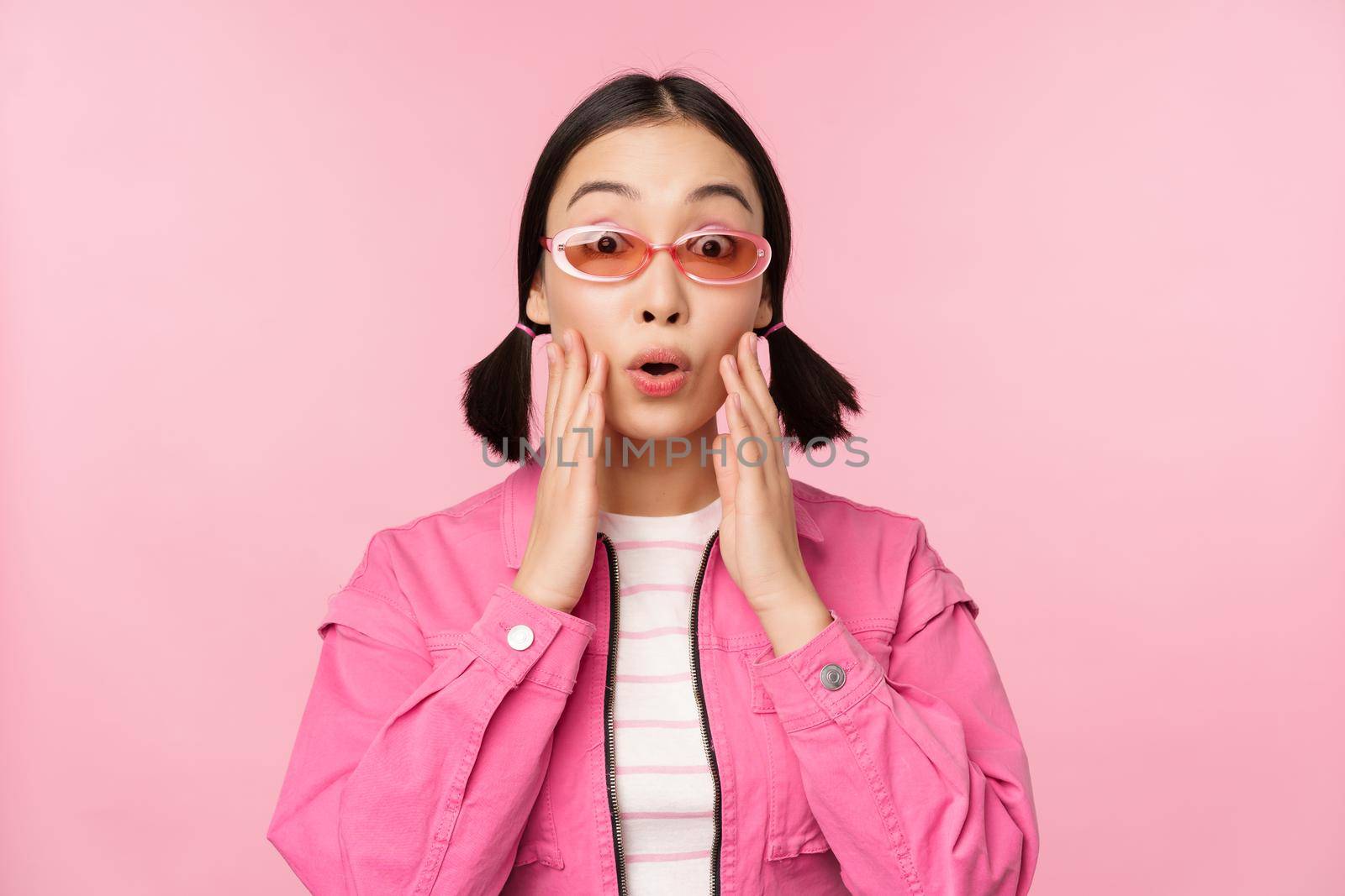 Image of asian girl looking surprised and excited, smiling, amazed reaction to big news, standing over pink background by Benzoix