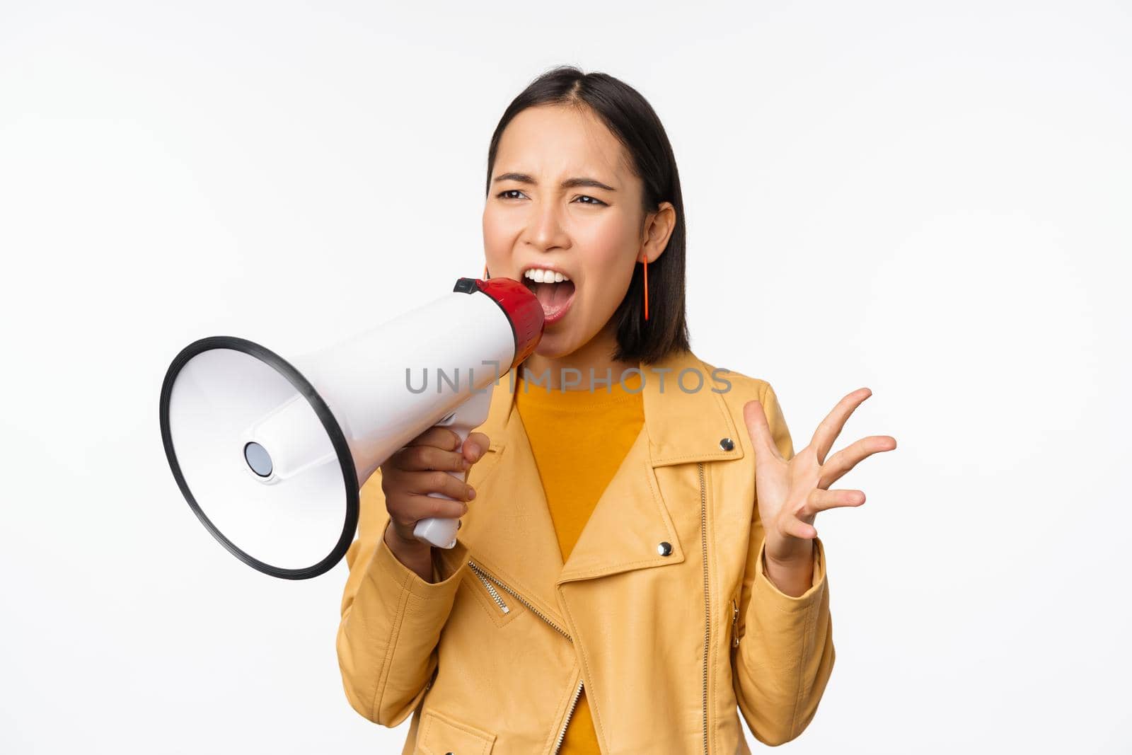 Portrait of young asian woman protester, screaming in megaphone and protesting, standing confident against white background.