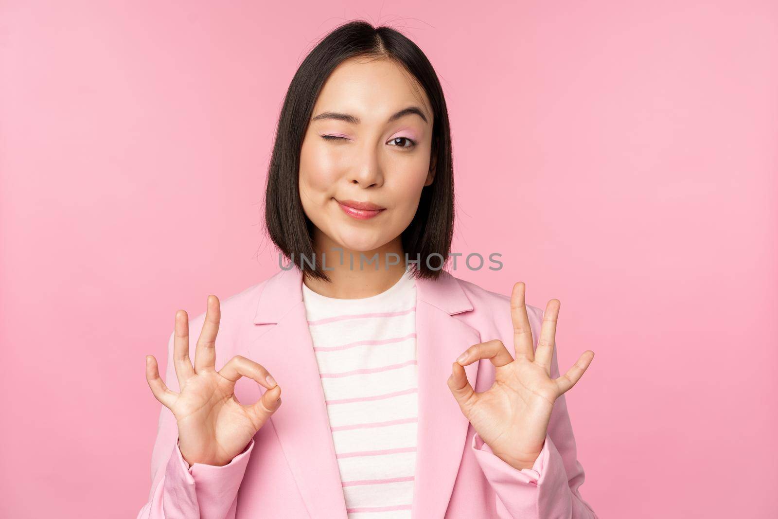 Okay, excellent. Businesswoman in corporate suit, showing ok, approval gesture, recommending smth, give positive feedback and smiling pleased, posing over pink background by Benzoix
