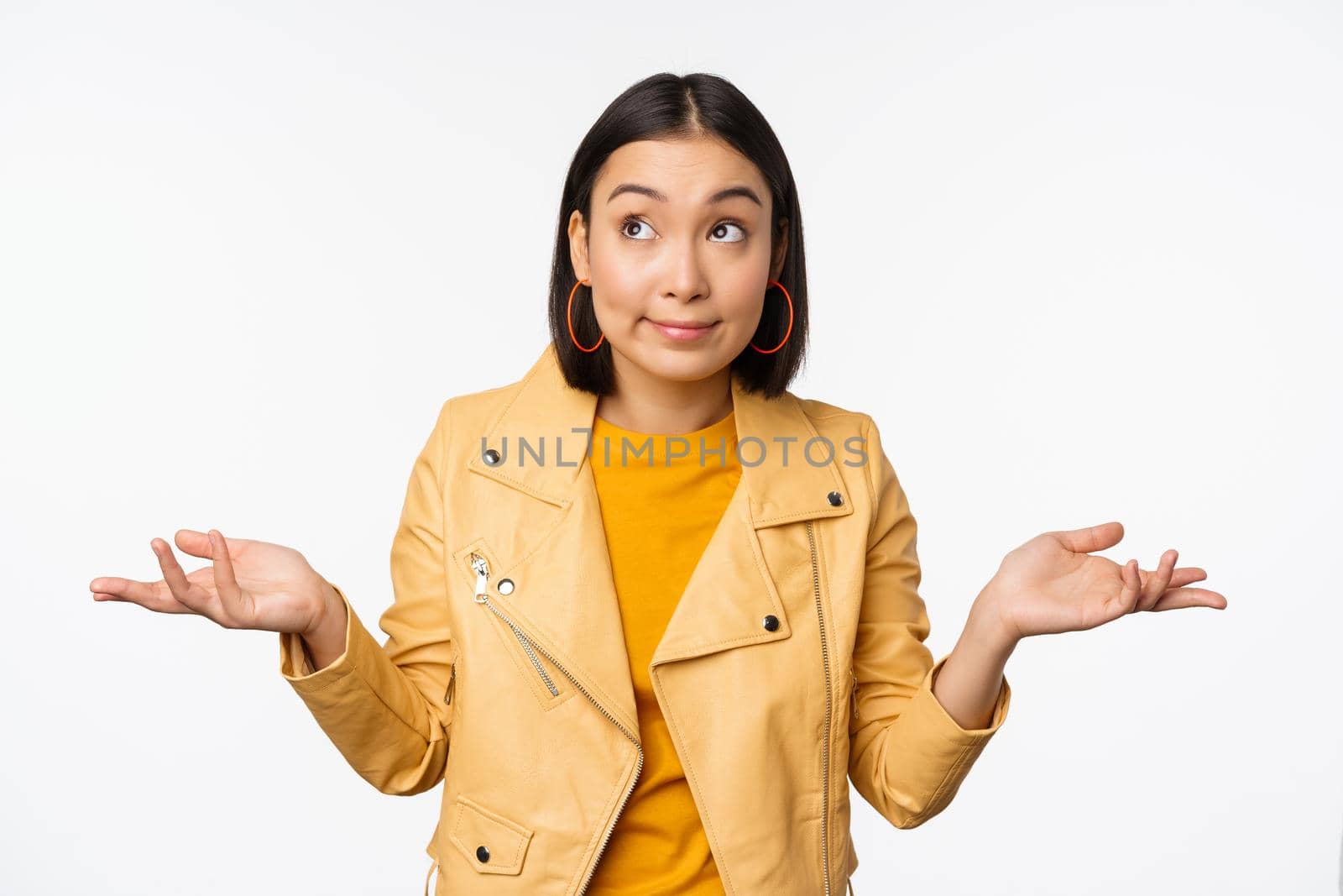 Image of korean girl shrugs shoulders and looks confused, dont know, cant tell, standing over puzzled over white background by Benzoix