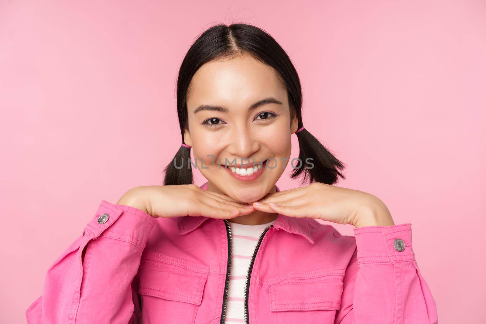 Skin care and cosmetology concept. Beautiful asian girl smiling and laughing, showing clean healthy facial skin, posing against pink background by Benzoix