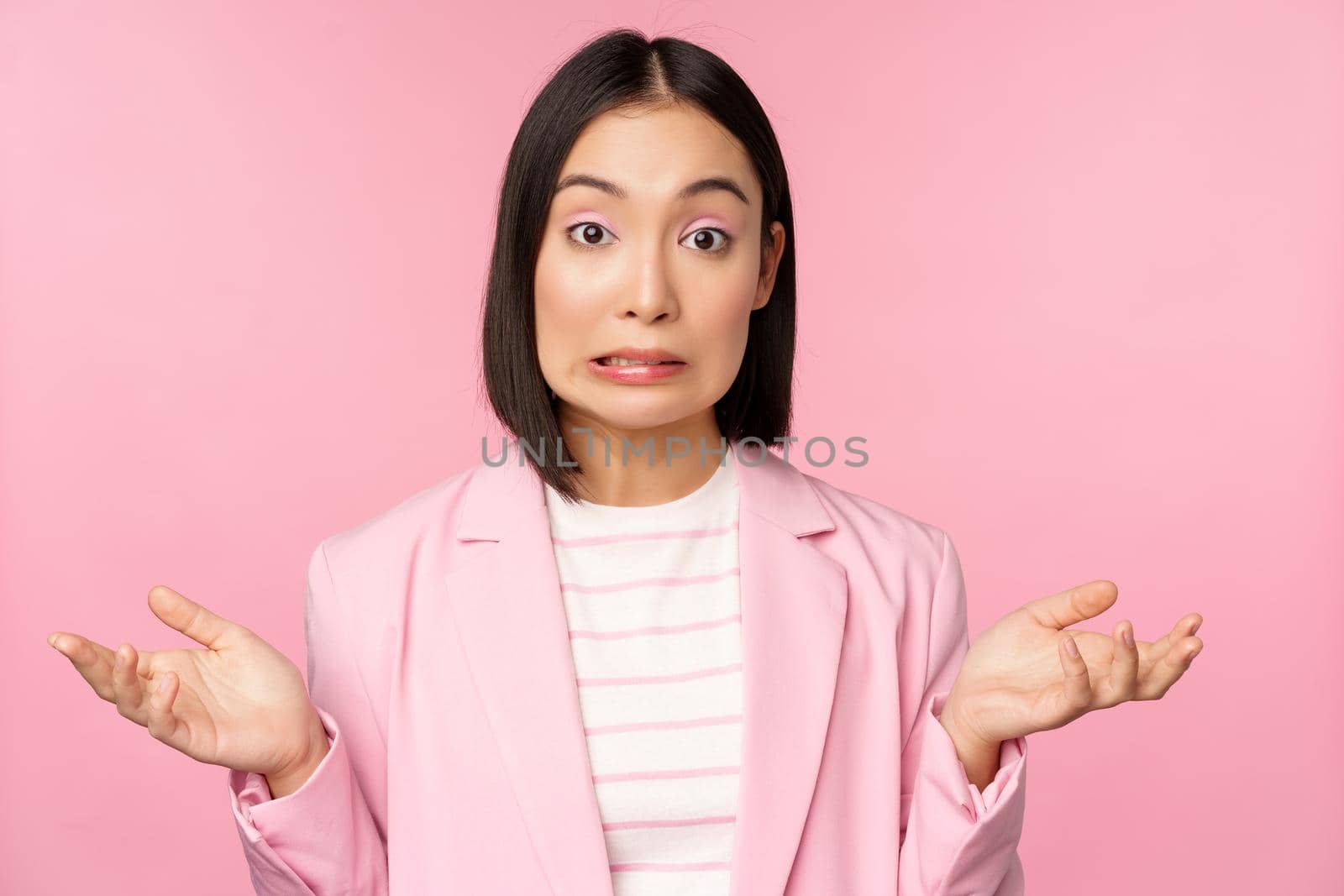 Portrait of confused asian businesswoman shrugging shoulders, looking clueless and puzzled, dont know, cant say, standing over pink background in office suit by Benzoix