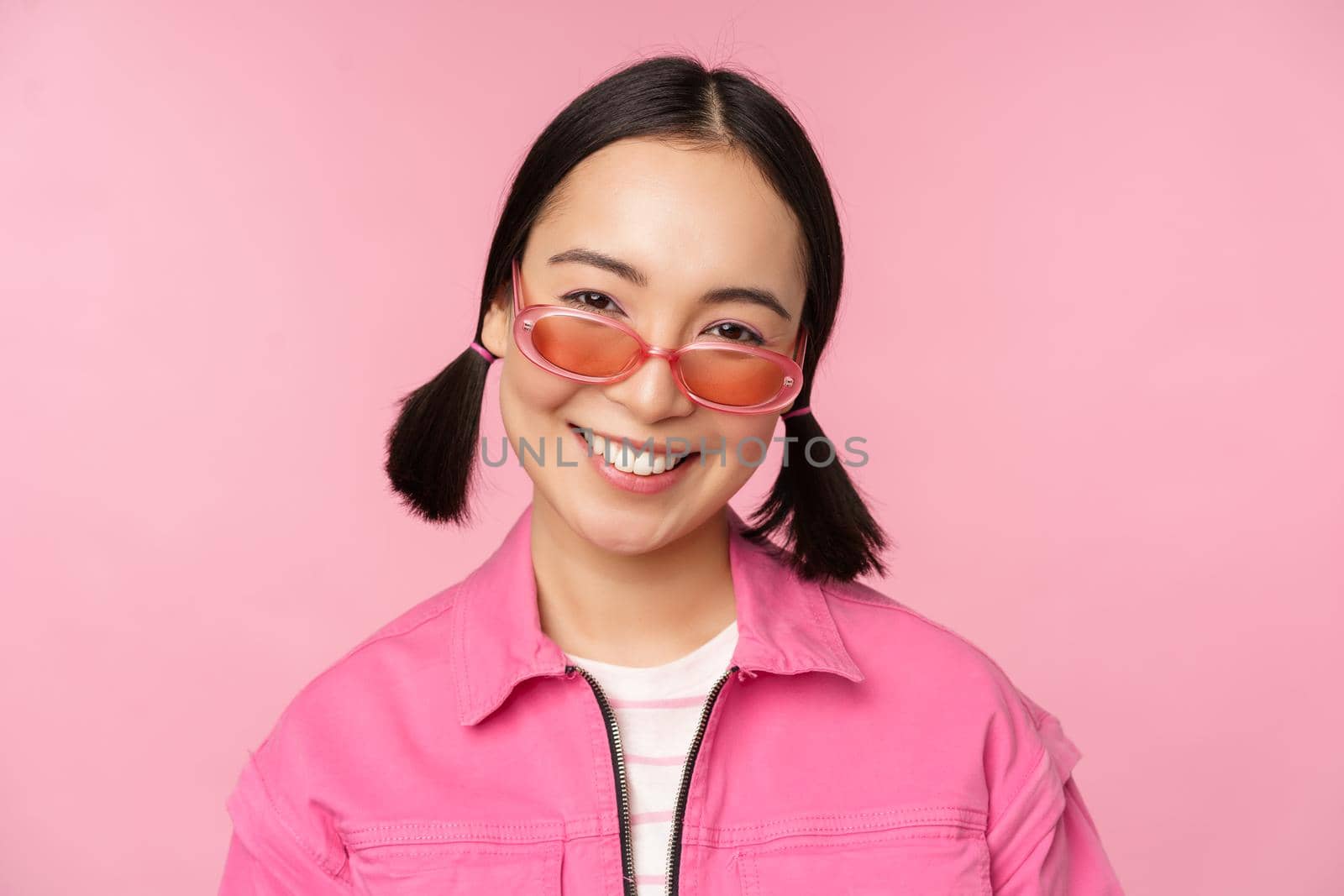 Close up of stylish korean girl in sunglasses, smiling happy, posing against pink background. People face concept by Benzoix
