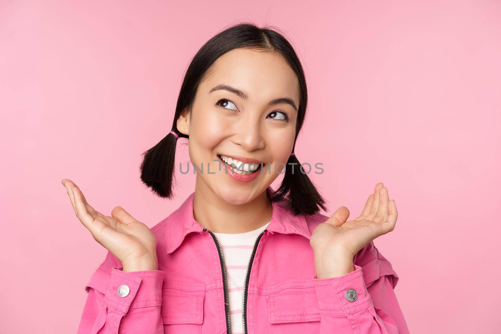 Skin care and cosmetology concept. Beautiful asian girl smiling and laughing, showing clean healthy facial skin, posing against pink background. Copy space