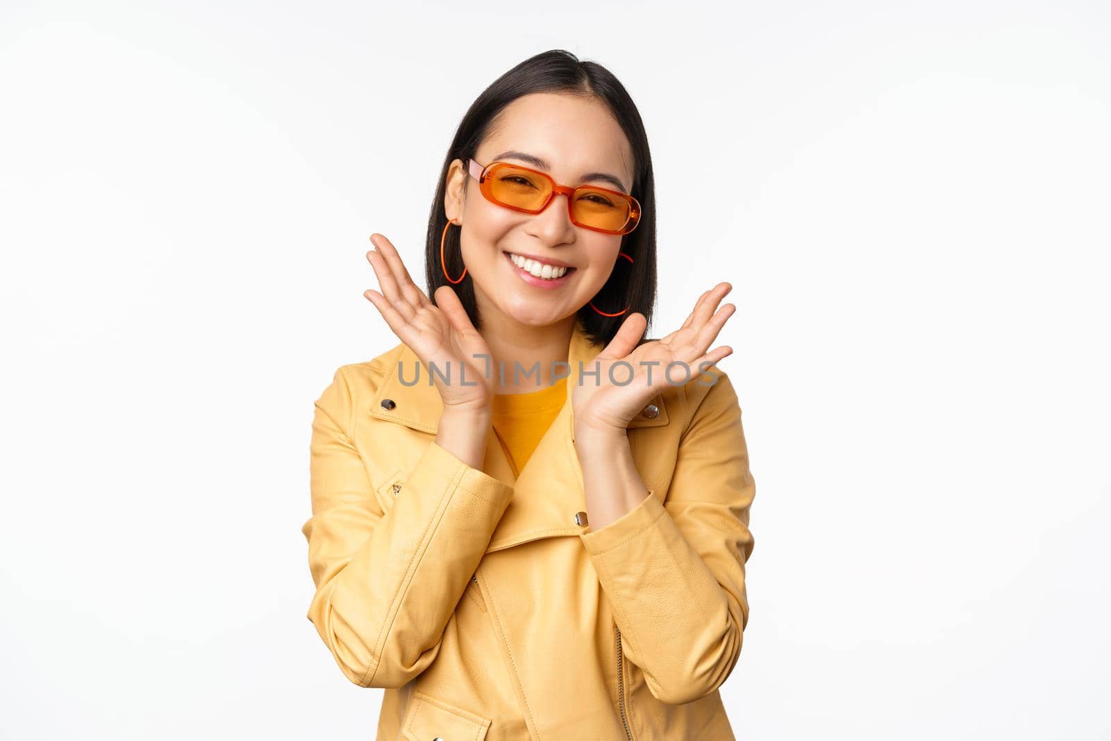 Beautiful asian girl in stylish sunglasses, smiling happy, looking bright and carefree, standing over white background by Benzoix