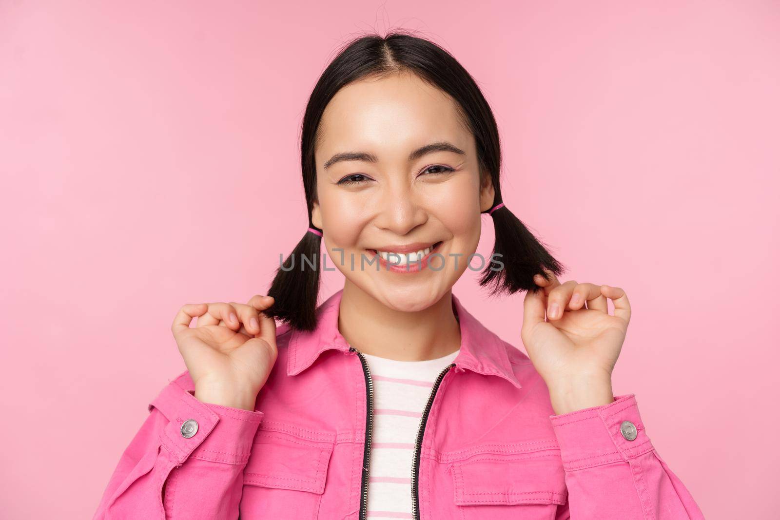 Skin care and cosmetology concept. Beautiful asian girl smiling and laughing, showing clean healthy facial skin, posing against pink background. Copy space