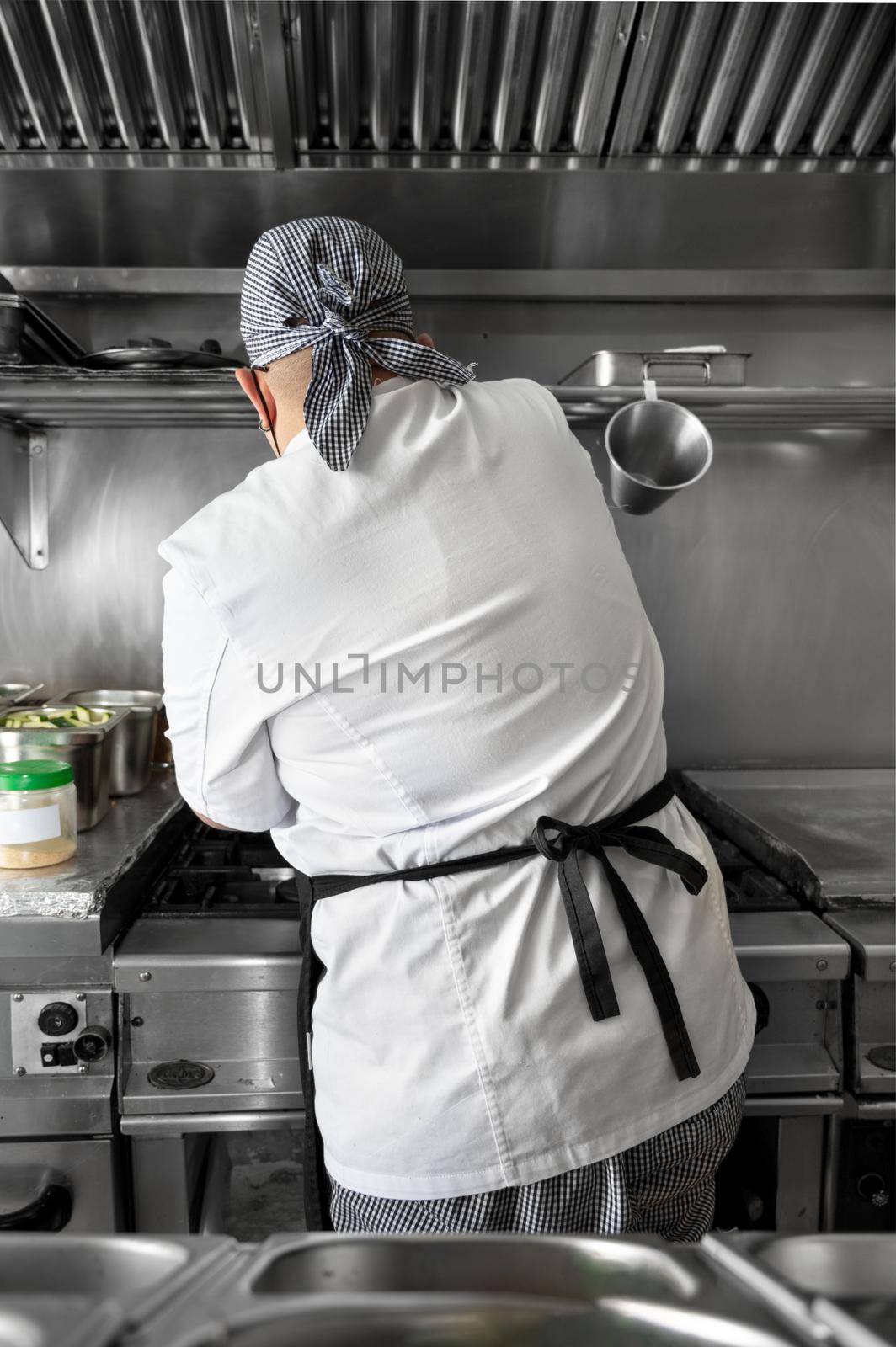 Back view of woman chef cooking food in the kitchen of a restaurant. by HERRAEZ