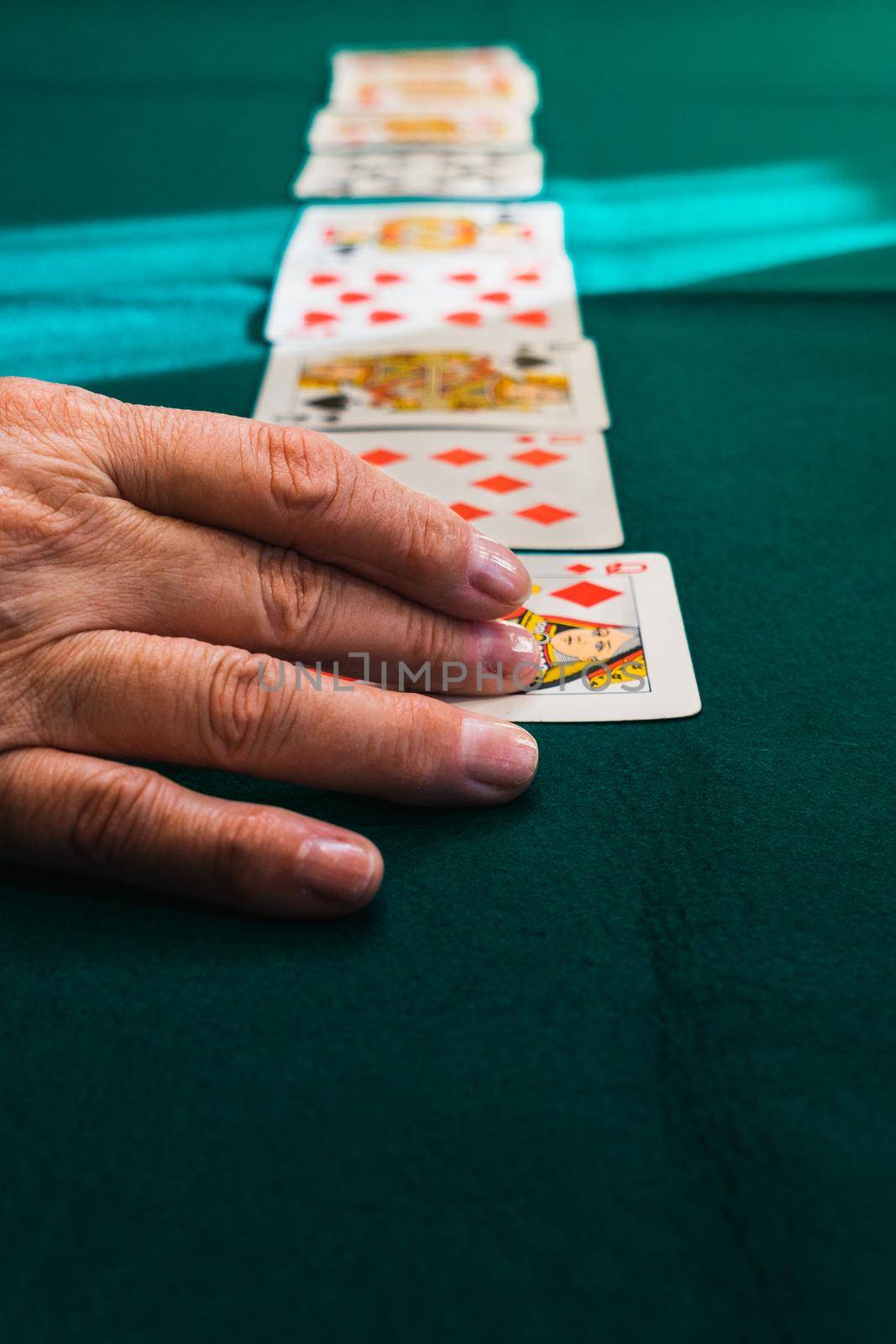 Granmother's hands playing a card game. Playing cards on a green mat. At the table at home, with natural light from the window. Zenithal shot of hands