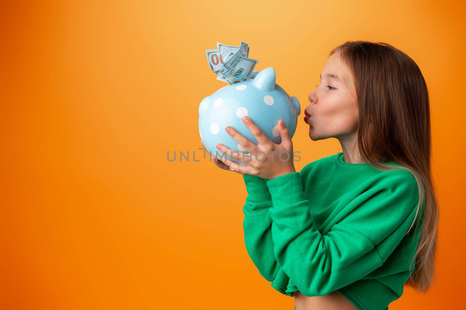 Teen girl with piggy bank on orange color background, portrait