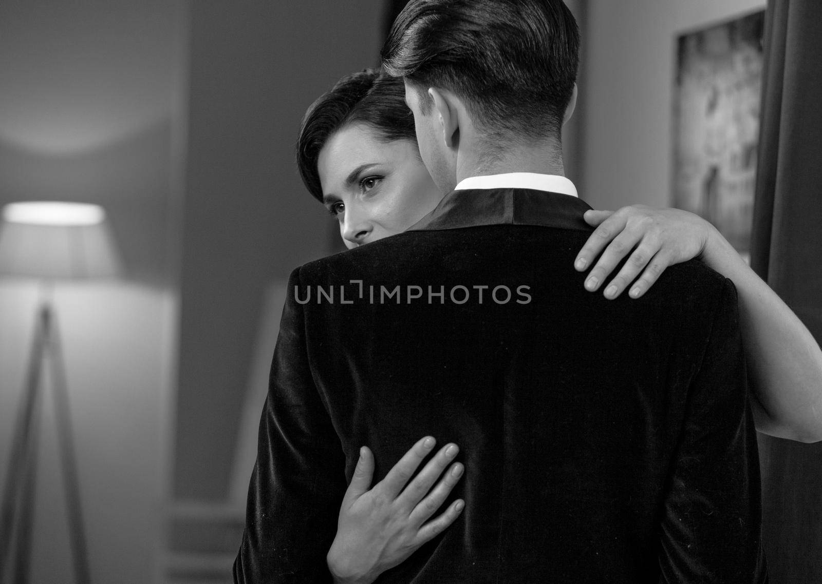 Dancing passion woman hugs man standing back to camera. Husband and wife after a romantic dinner. Romance in relationships. Beautiful young couple in home interior. Black and white photo.
