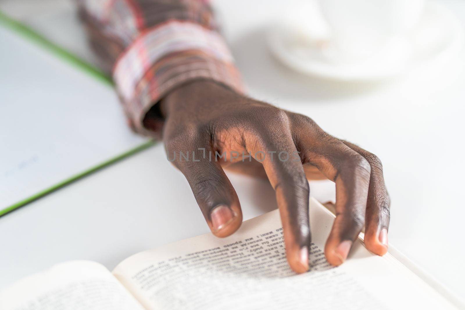 Close up on young male hand of african american man reading book making notes. Student preparing to the lecture at library reading books and making notes. Adduction concept.