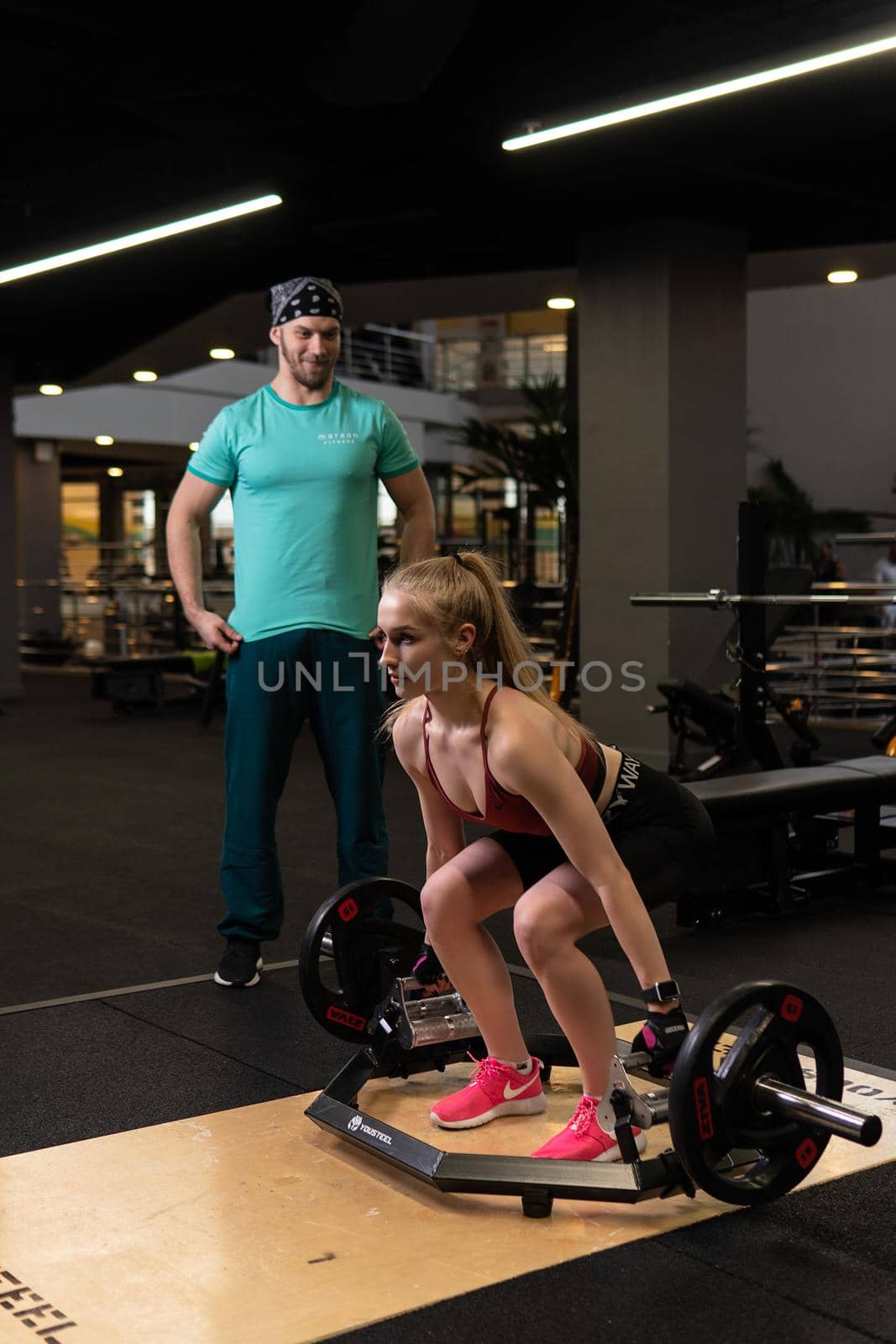 RUSSIA, MOSCOW - FEB 11, 2022: Instructor and client girl deadlift blonde trap bar personal teach, from instructions motivation for person for power trap, giving lift. Heavy coach bodybuilding, active by 89167702191