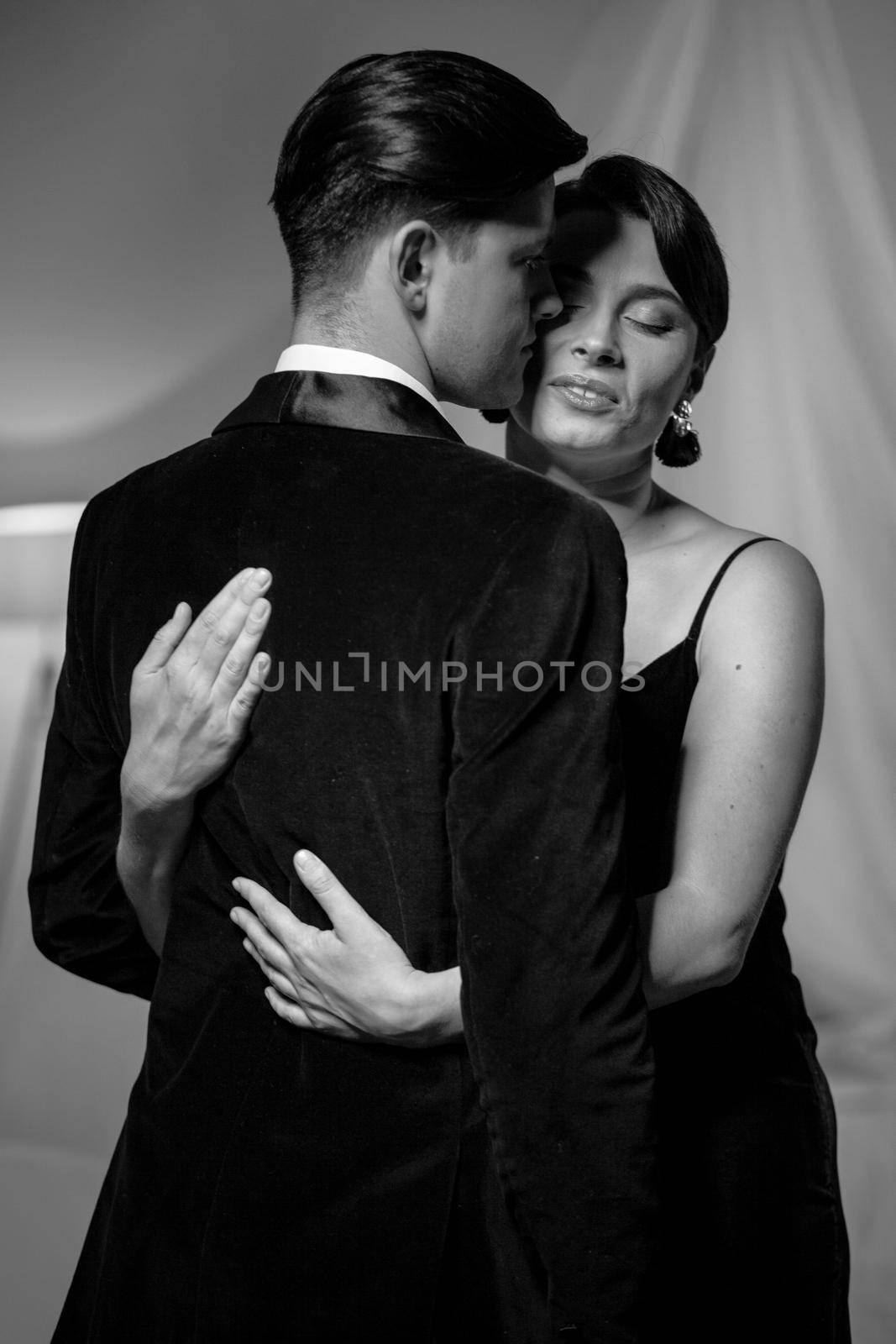 Passion in love woman hugs man standing back to camera. Husband and wife after a romantic dinner. Romance in relationships. Beautiful young couple in home interior. Black and white photo by LipikStockMedia