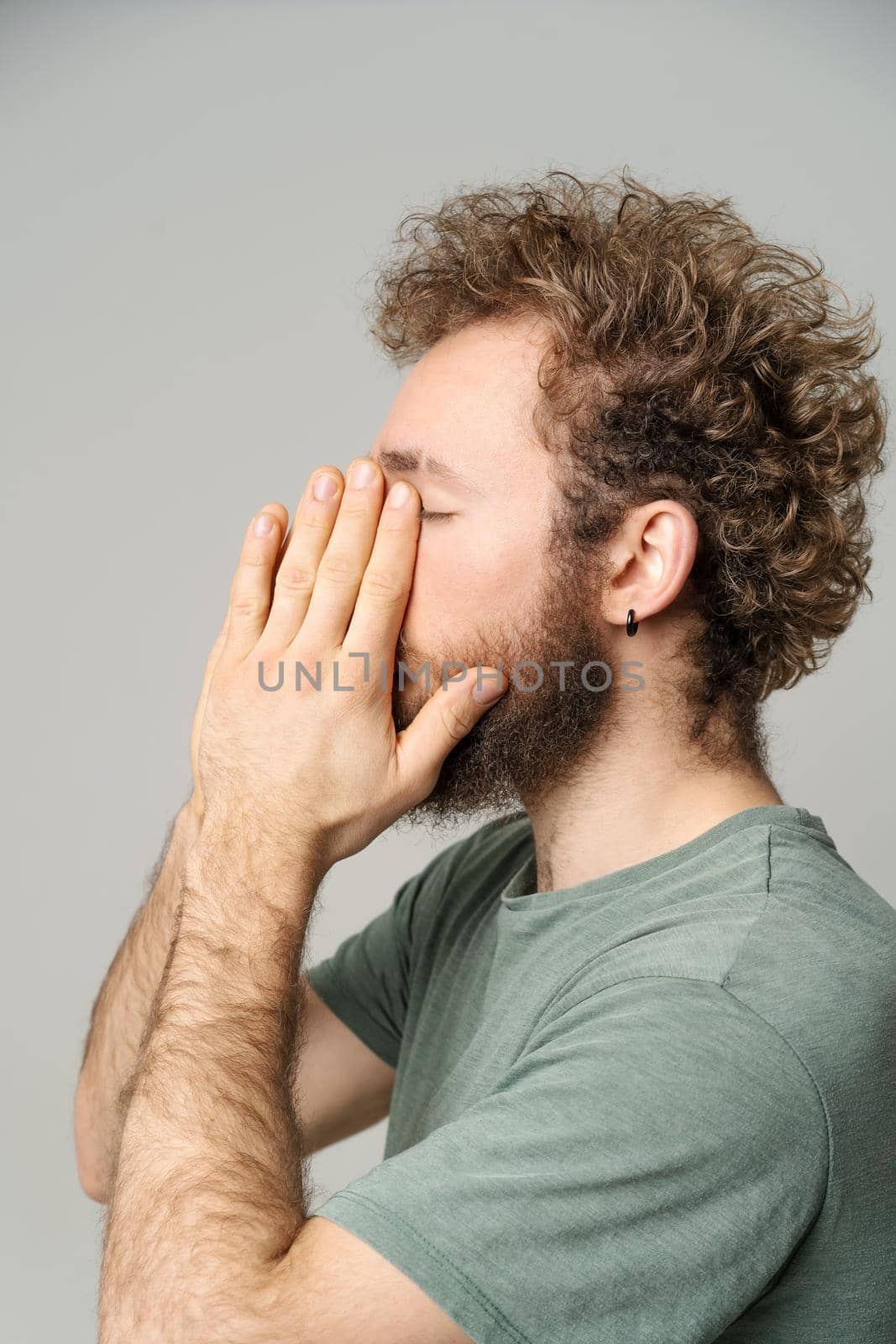 Young curly haired man hide face in hands tired, migraine concept. Handsome guy feel pain or headache. Frustrated young man trying to concentrate massaging his face. Health care concept.