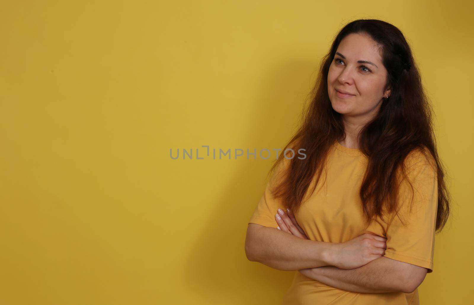 Beautiful woman in yellow t-shirt with long dark hair on yellow paper background. Pleasant brunette on a yellow background.