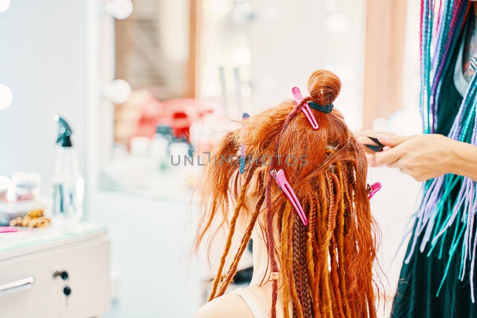 Barber braids dreadlocks. The hairdresser weaves braids with red kanekalon beautiful red-head girl. Beautiful cool hairstyles. Hair service in a beauty salon. Fashionable women's style.