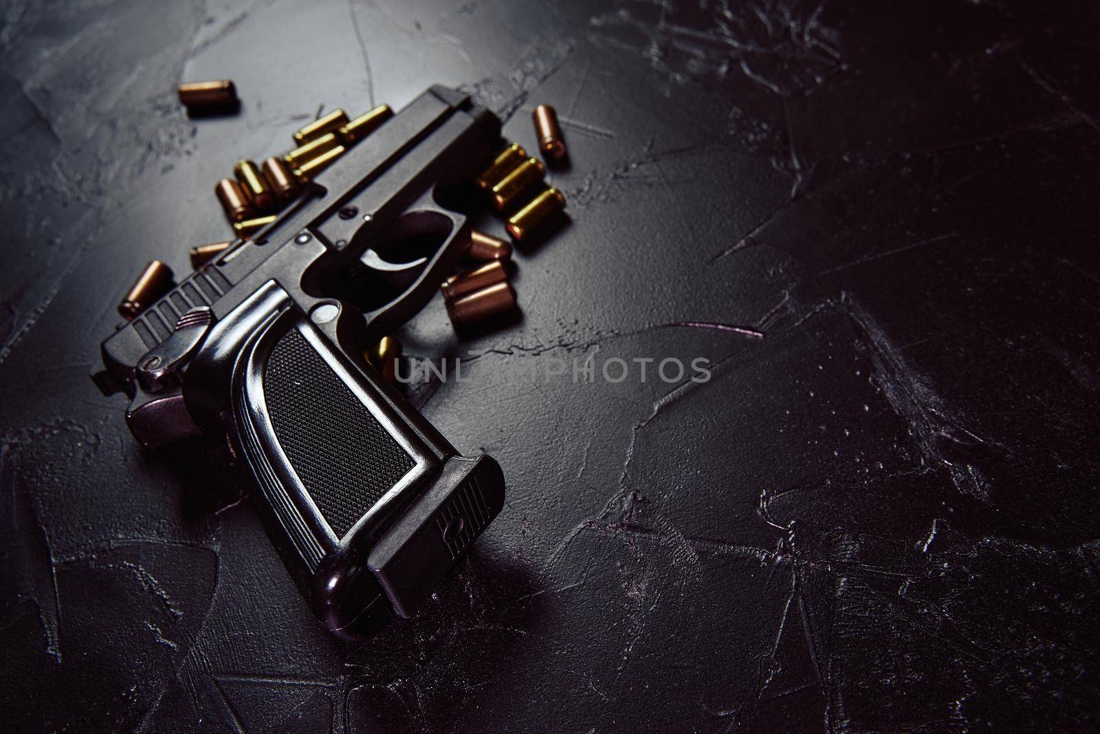 Black pistol with cartridges on table. Firearms on dark concrete table. Weapon of crime or defense. Automatic gun with bullets. Close up with copy space for text.