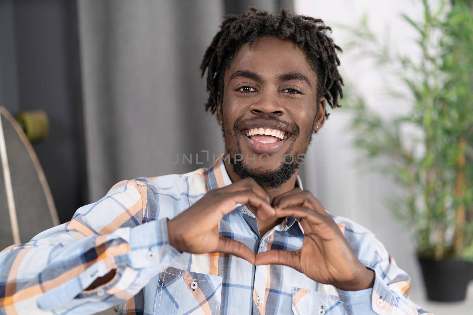 Charming african man in plaid shirt send love sign gesturing it with hands. African american male model makes love figure by his hands.High quality photo.