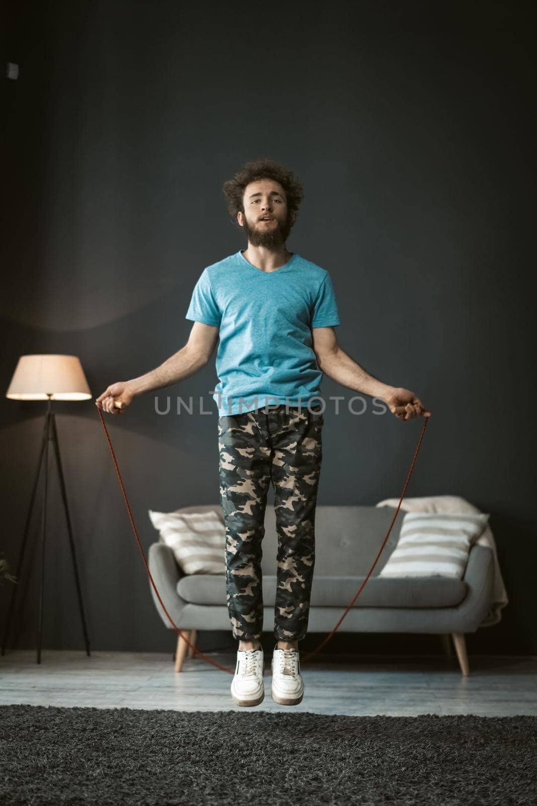 skipping rope jumping young man working out at home. Young man on self isolation or quarantine, pandemic days. Handsome curly hair man use skipping rope to stay fit and healthy.